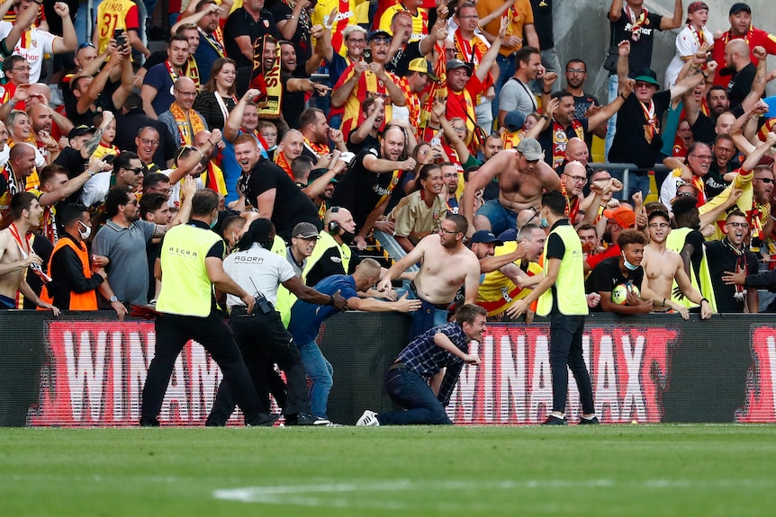 Un groupe de fans de football français trébuche sur le terrain, entouré de gardes de sécurité lors d'un match de championnat.