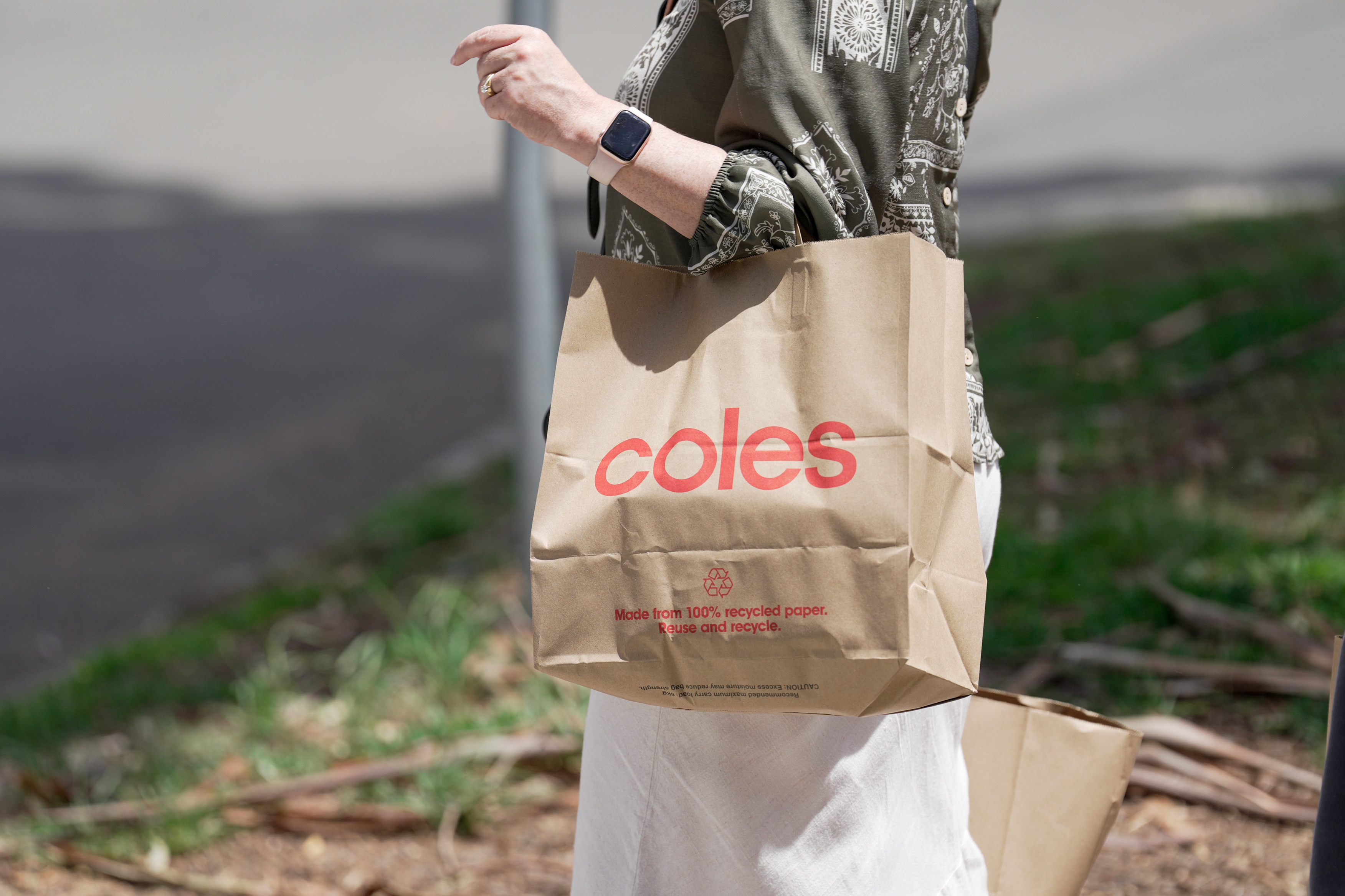 A person walking with a brown paper bag on their arm with the word Coles.