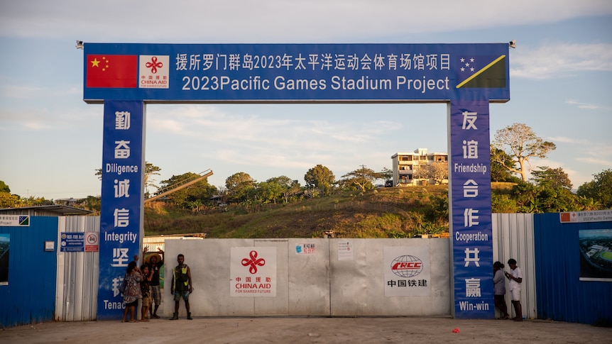A construction site gate with China and Solomon Islands' flags and "2023 Pacific Games Stadium Project" in English and Chinese.