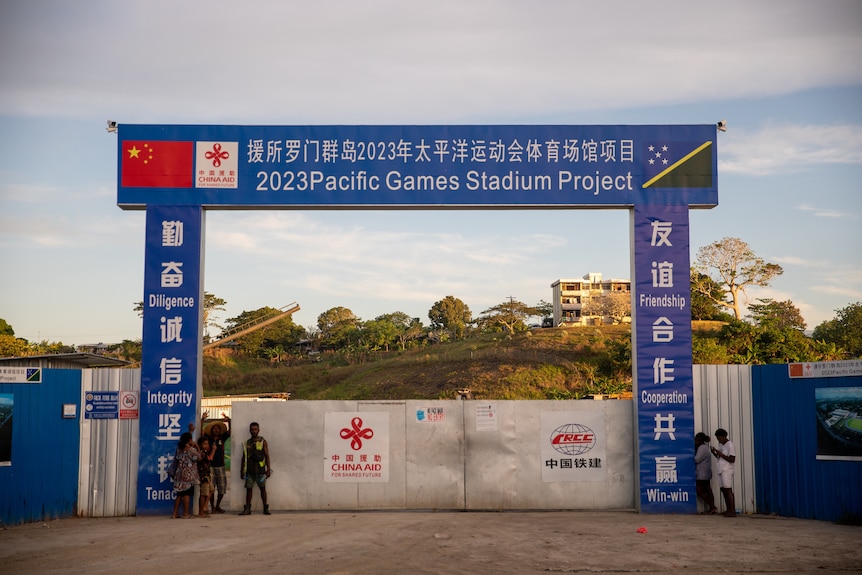 A construction site gate with China and Solomon Islands' flags and "2023 Pacific Games Stadium Project" in English and Chinese.