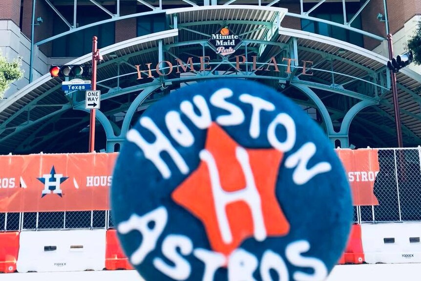 A cookie reading Houston astros is held up against minute maid stadium