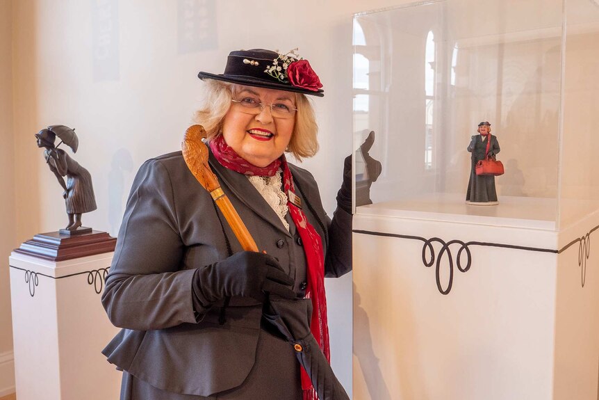 Woman dressed as Mary Poppins stands next to small model of herself.