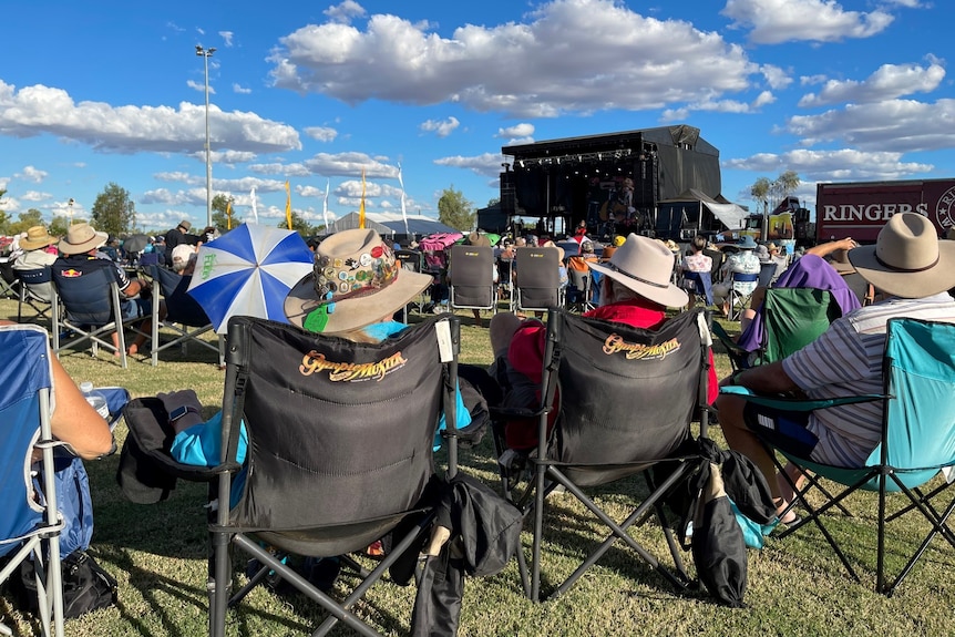 Festival goers sit in camp chairs and watch music acts perform on main stage