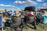Festival goers sit in camp chairs and watch music acts perform on main stage