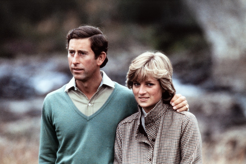 Prince Charles, wearing a green sweater over a shirt, puts his arm around Diana, in a checked coat