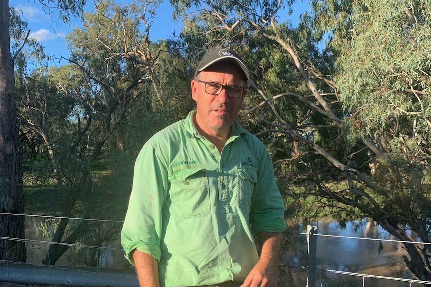 Simon Logan wearing a green Landmark shirt standing in front of some gumtrees and a creek.