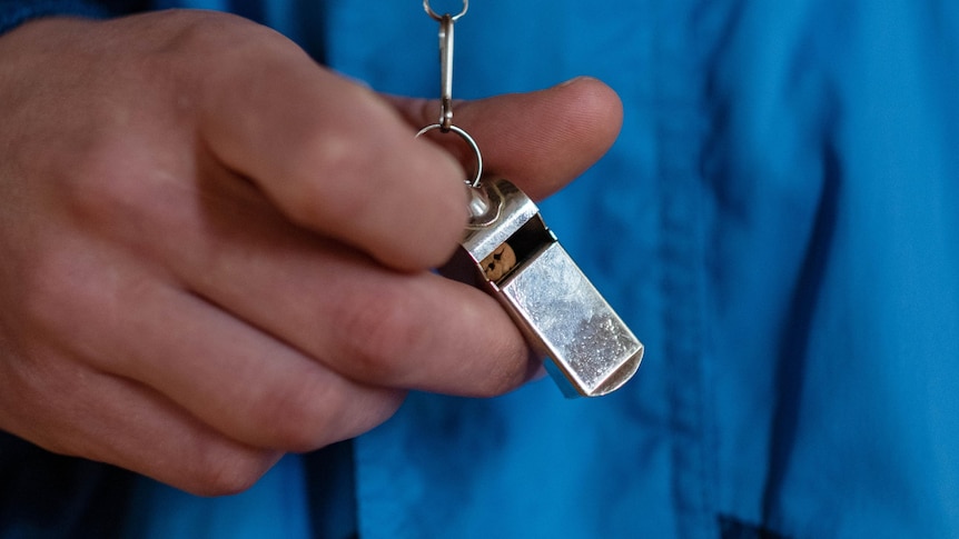 A close up photo of a man in a blue jacket holding a silver whistle