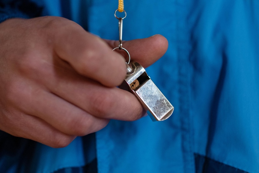 A close up photo of a man in a blue jacket holding a silver whistle
