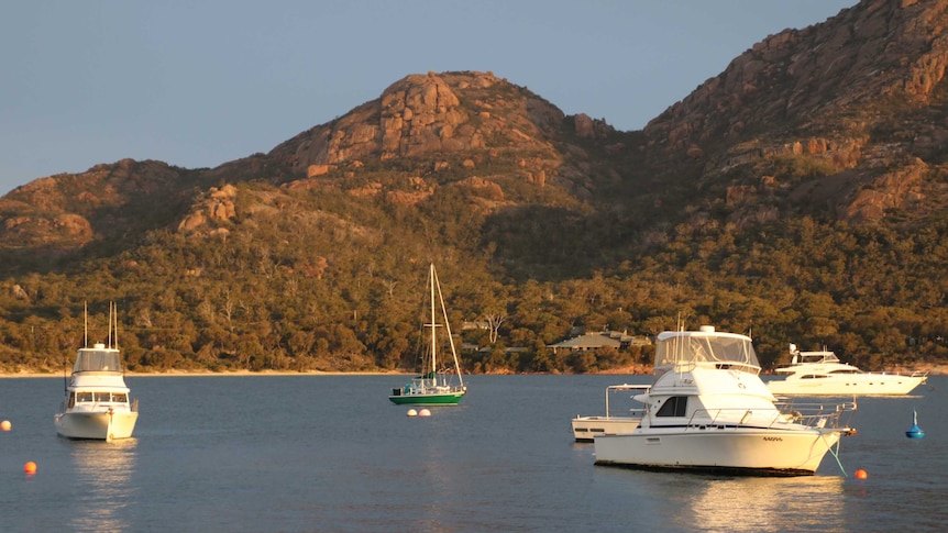 Boats moored in a bay with red granite peaks in the background.