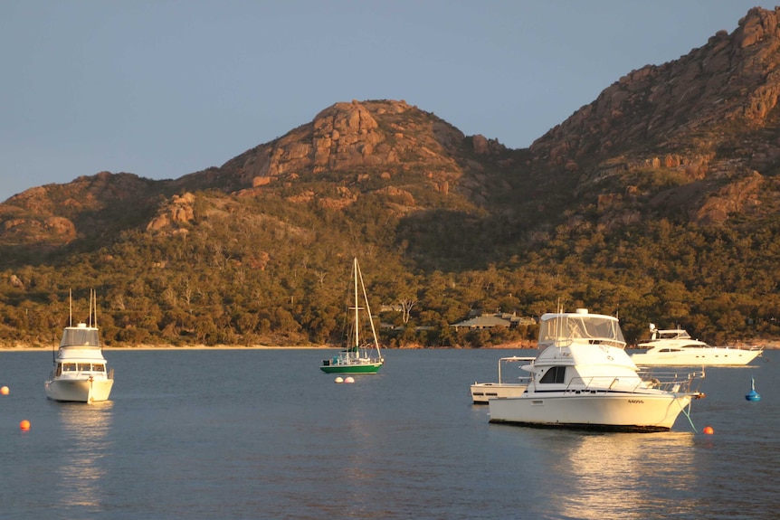 Boats moored in a bay with red granite peaks in the background.
