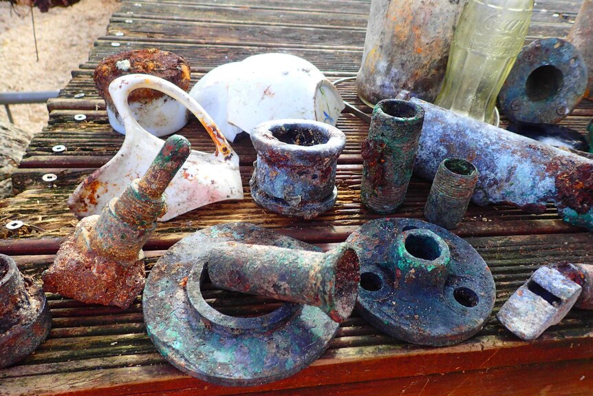 Rusted metal fittings sit on a table at the beach.