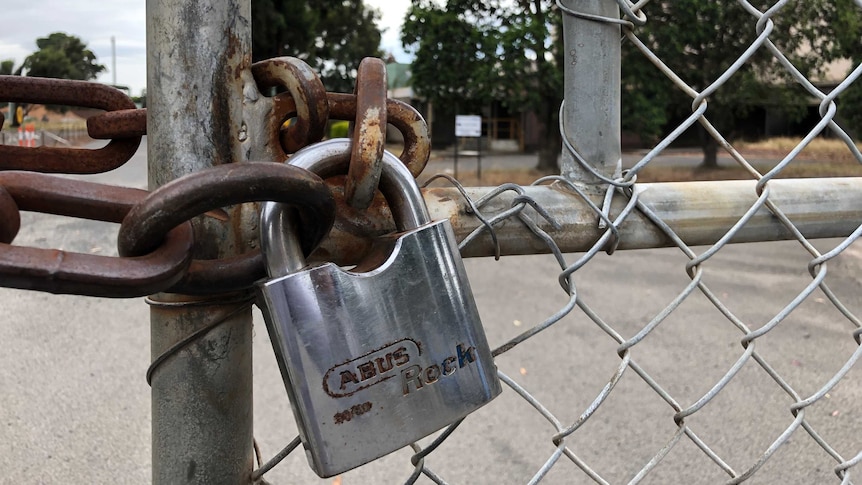 A rusty lock and chain on a gate at a closed factory