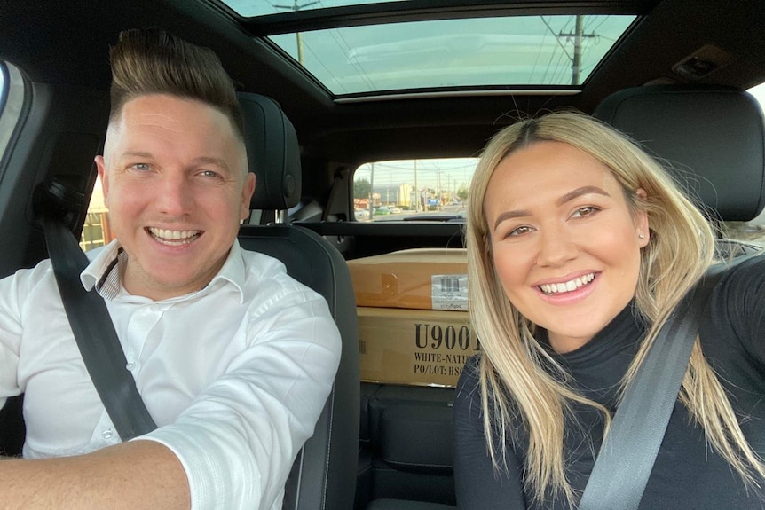 Pietro and Sarah Bertolini in a car with their new baby cot in a cardboard box on the back seat.