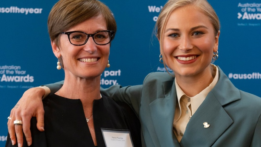 Close up photo of two women smiling at the camera standing in front of the Australian of the Year Awards banner