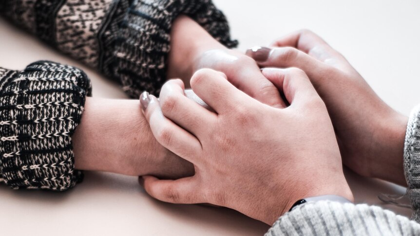 Two pairs of hands reach across the table and clasp together, they are wearing jumpers.