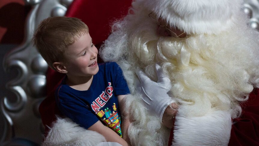 A little boy reacts in conversation on Santa's knee.