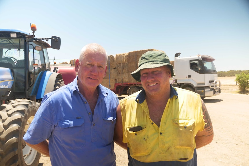 Two volunteer truck drivers stand in front of a hay truck.