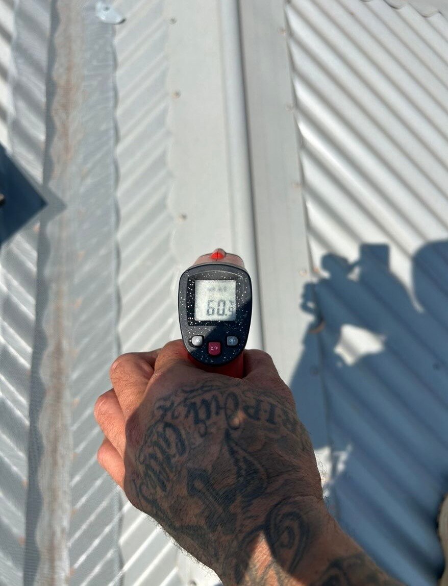A hand is holding a temp gun on a hot tin roof - it reads 60.9 degrees Celsius
