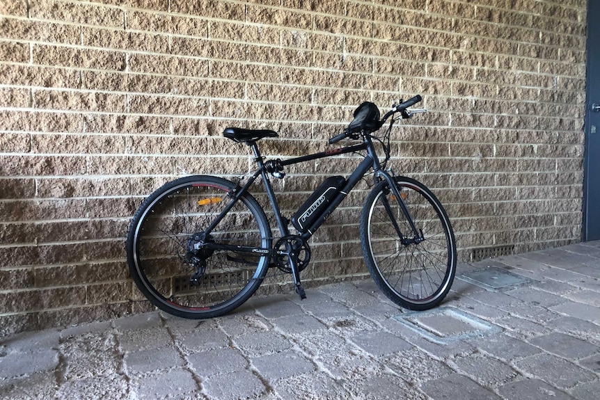 A black electric bicycle in front of a wall.