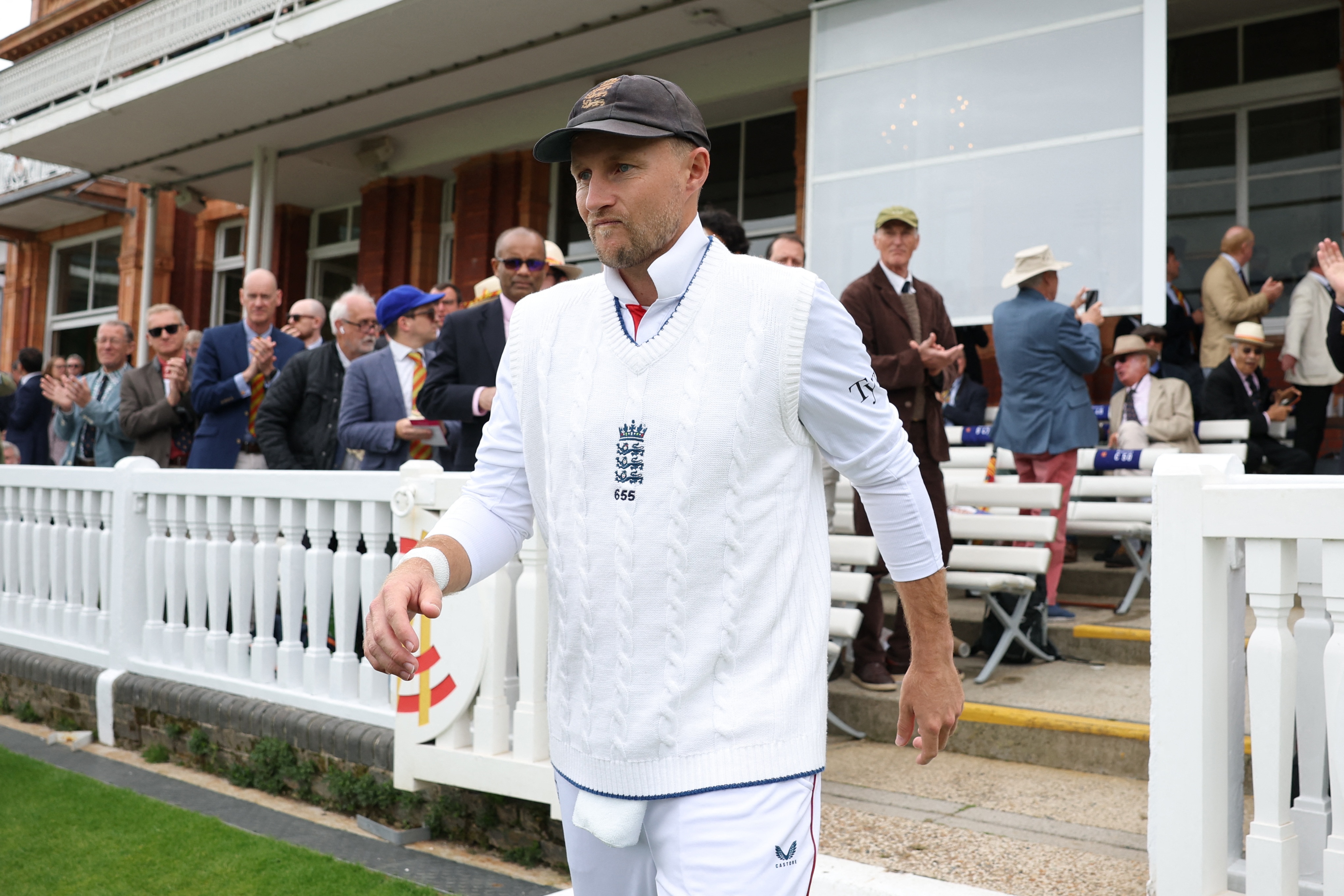 Joe Root walking onto a cricket field with spectators standing behind him.