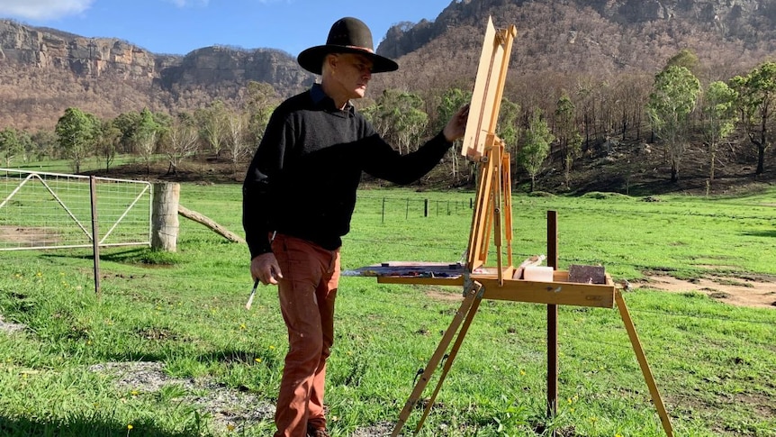 Warwick Fuller paints with mountains in the background.