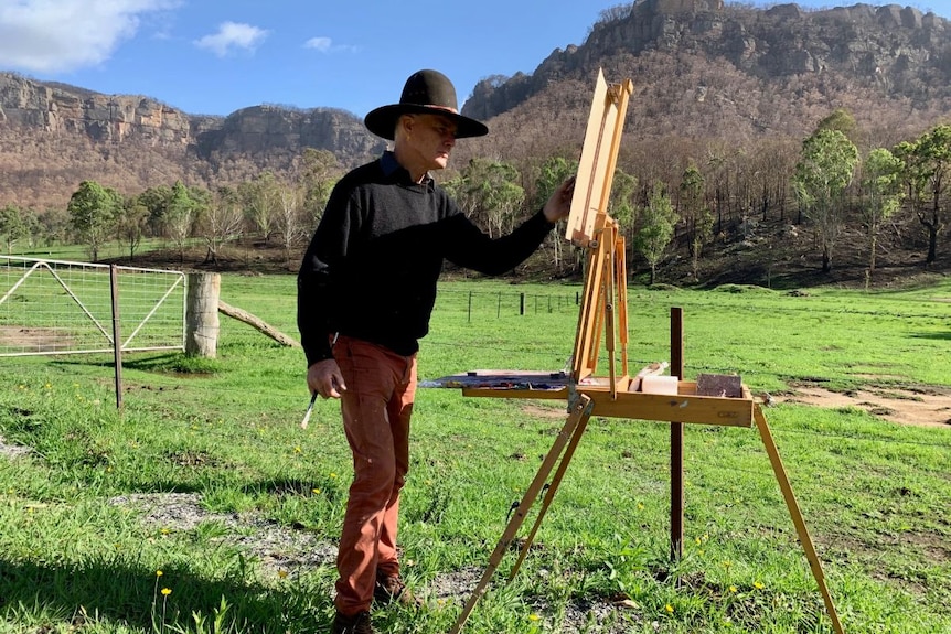 Warwick Fuller paints with mountains in the background.