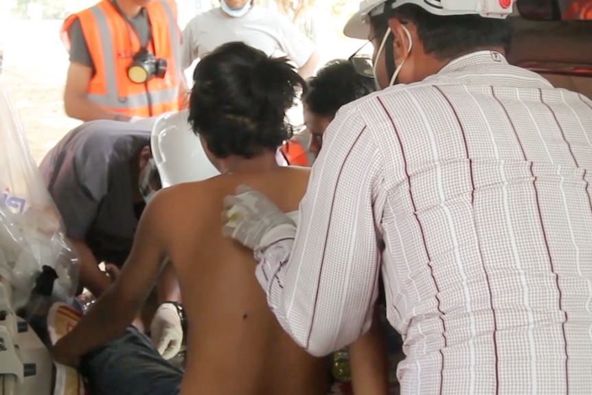 A man treats a boy's back while wearing a mask.