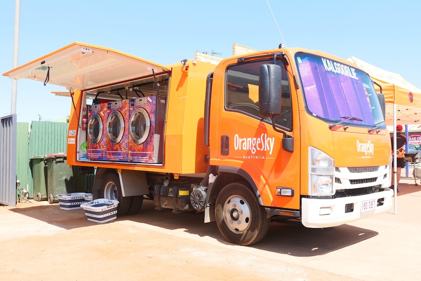 an orange bus with three washing machine on the tray 