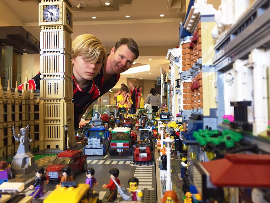 A man and a child look towards the camera, down a Lego street.