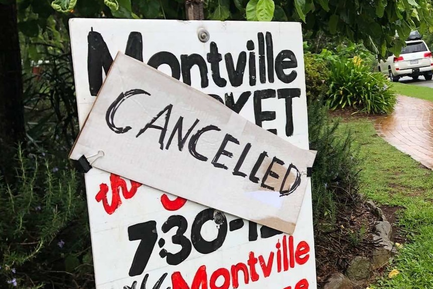 Hand-painted market sign with "cancelled" written across it, with greenery and old red phone box behind