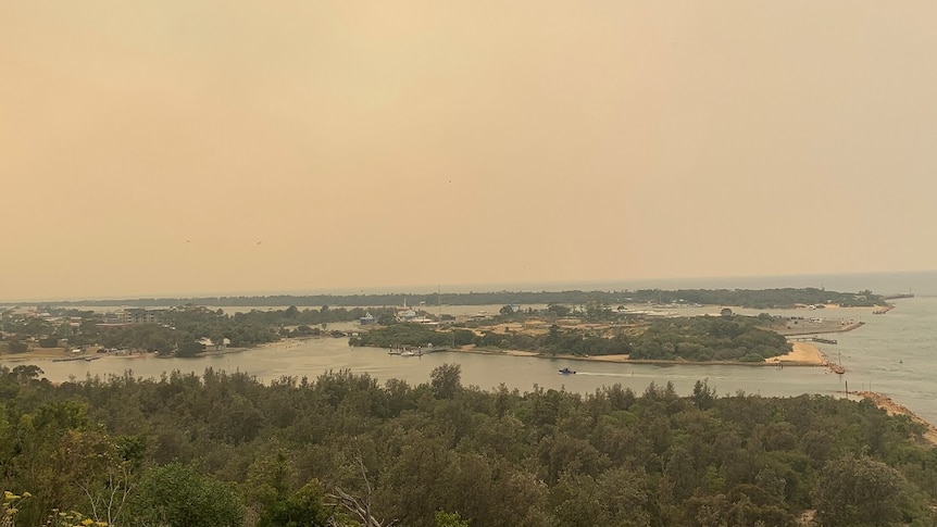 An orange haze hangs over the sky in a photo overlooking the coastal town of Lake Entrance.