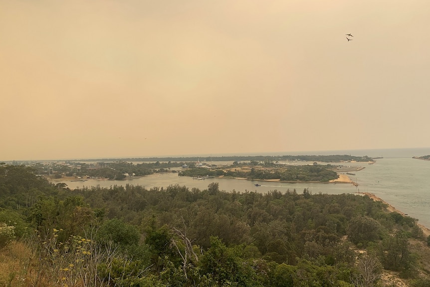 An orange haze hangs over the sky in a photo overlooking the coastal town of Lake Entrance.