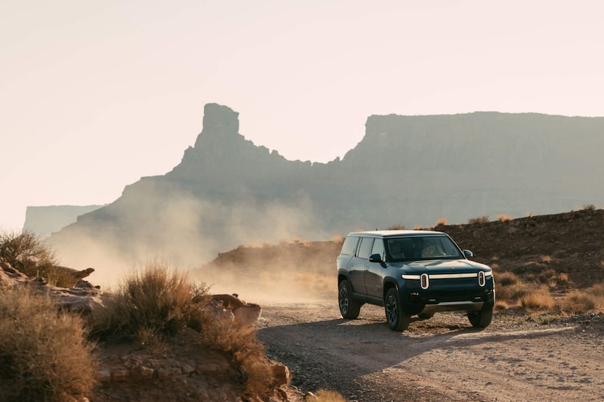 Black SUV drives on a dirt road through the desert.
