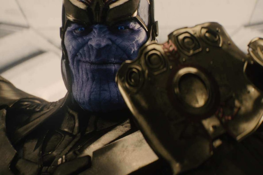 Thanos, a purple titan in gold armour, holds the golden Infinity Gauntlet.