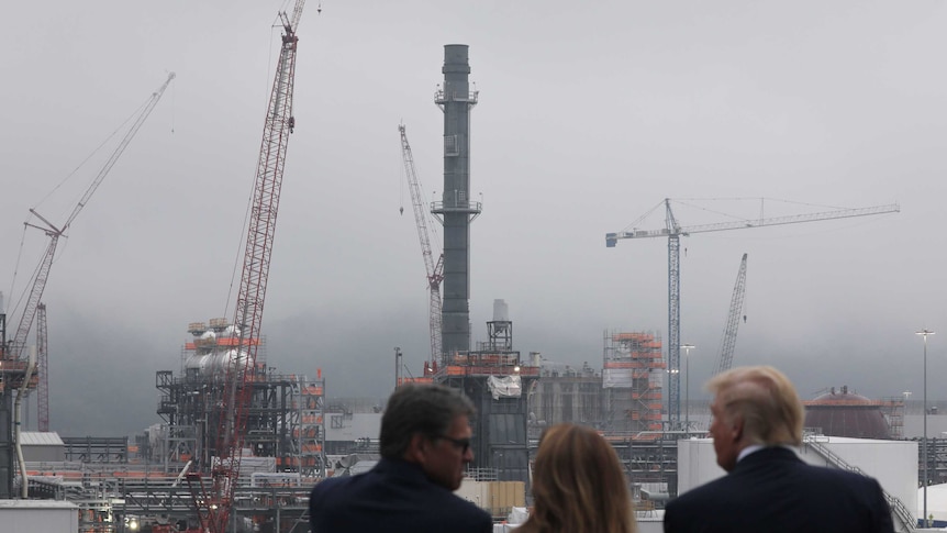 Three people stand overlooking a site with five cranes and structures being built.