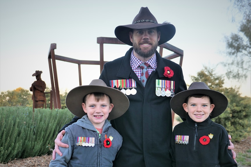 A man with a cowboy hat stands with two smaller children with hats. They are all wearing war medals.