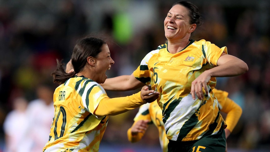 Two members of the Matildas leap in the air with joy to celebrate a goal.