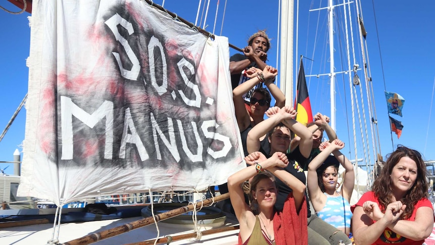 Group of activists in front of wooden sail boat with aboriginal flag.