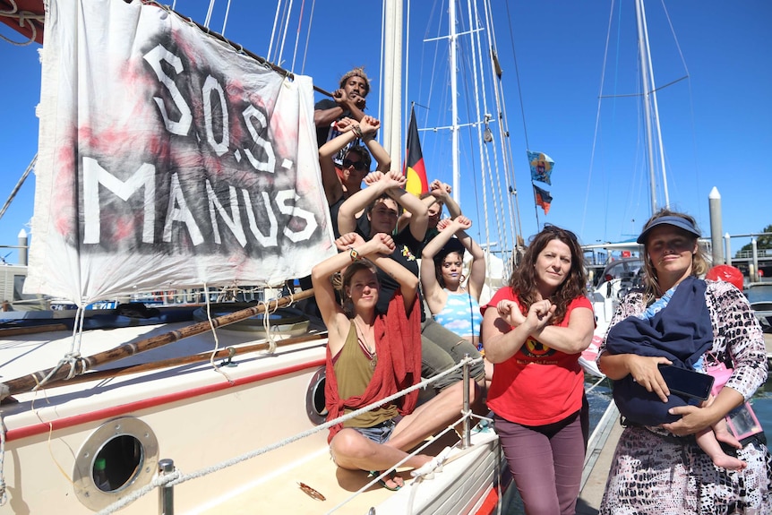 Group of activists in front of wooden sail boat with aboriginal flag.