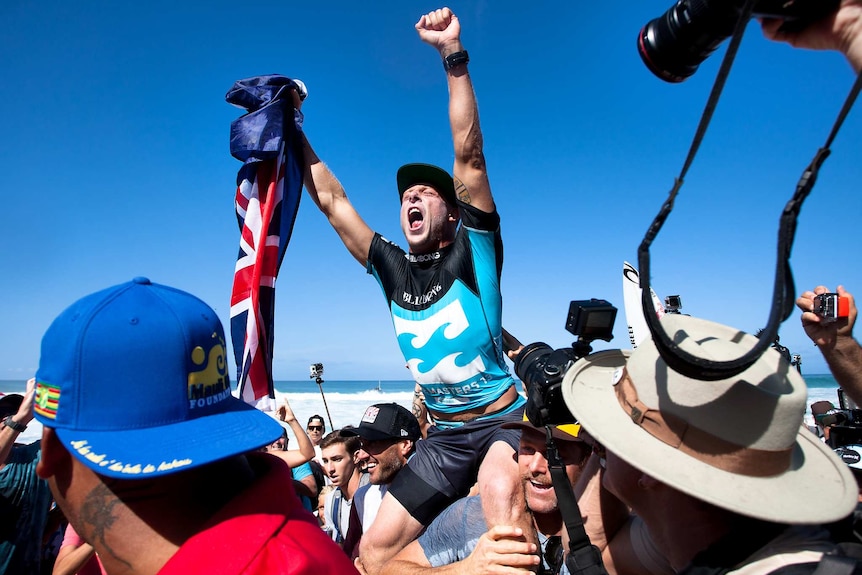 Surfer Mick Fanning celebrates with his arms in the air as he is carried aloft.