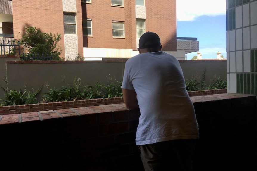 A man leans on a low brick wall, with his back to the camera.