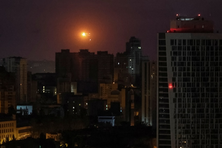 An explosion is seen in the sky over Kyiv,with a bright orange ball haning in dark dawn sky over high rise buildings.