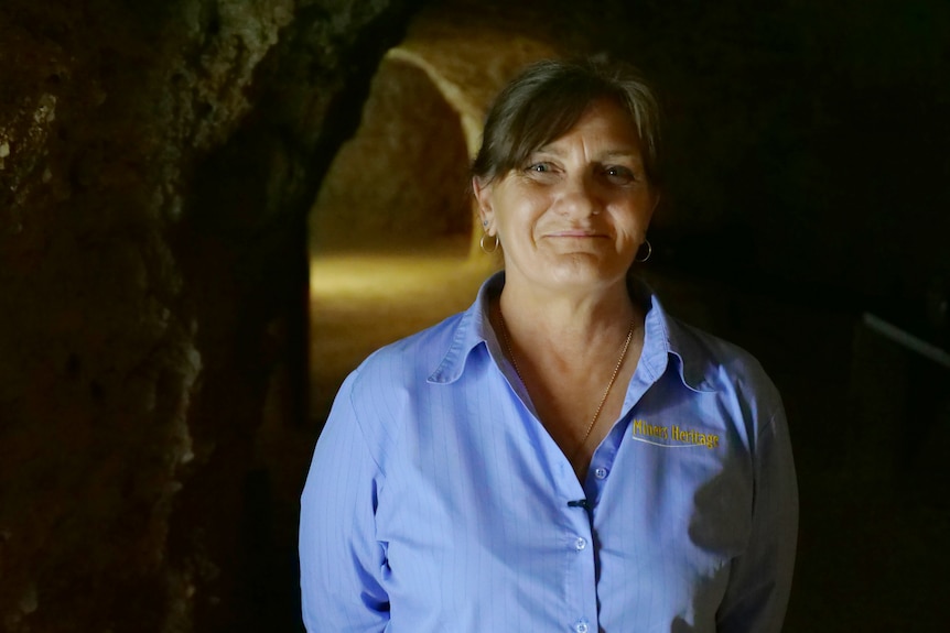 Michelle smiling, wearing a blue top, dark caves behind her.