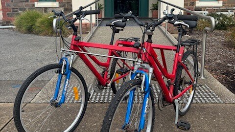 two red bikes joined together to become a tandem bike on a path in front of a building archway