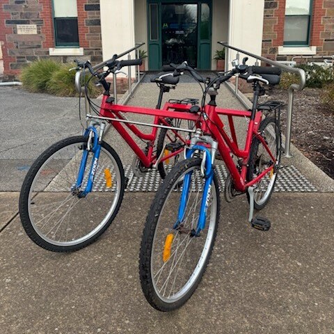 two red bikes joined together to become a tandem bike on a path in front of a building archway