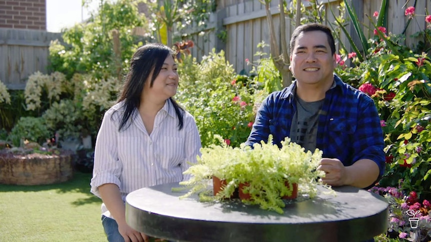 A man and a woman sitting at an outdoor table in a garden.