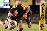 A Penrith NRL player dives in the air holding the ball with his right hand as he attempts to score a try while being tackled.