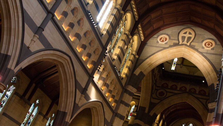 Inside of a sandstone cathedral, stained glass windows, high arched ceiling.
