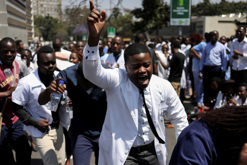 A man in a white coat holding his hand up at a protest