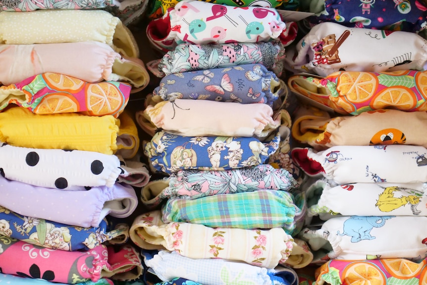 a box full of brightly patterned cloth nappies, all stacked neatly.